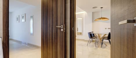 Un interior moderno con una puerta de madera, una zona de comedor con mesa y sillas, y una lámpara colgante.