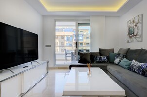 Una sala de estar moderna con un televisor de pantalla plana, una mesa de centro blanca y un sofá gris con cojines estampados.