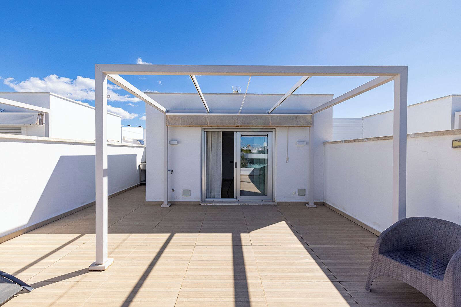 A rooftop terrace with a covered seating area, a sliding glass door entrance, and a view of the cityscape.