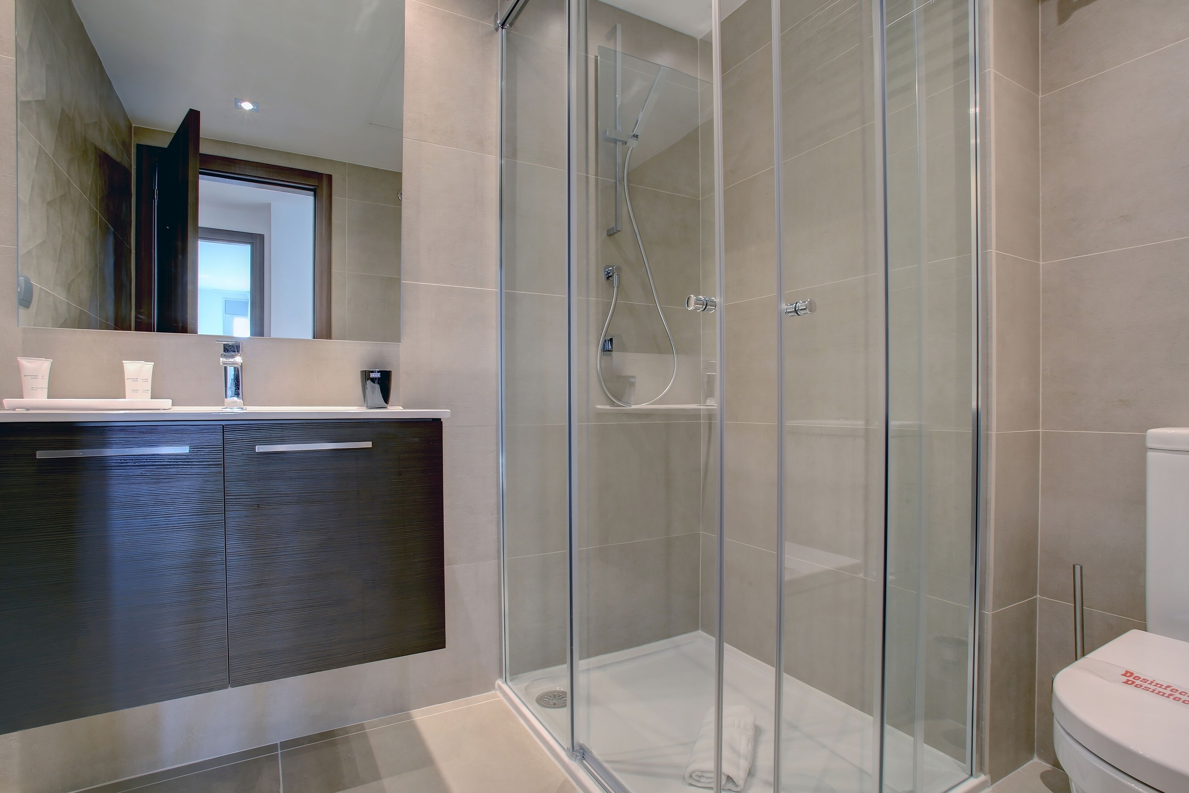 Un baño moderno con ducha acristalada, muebles de madera oscura y un inodoro blanco.