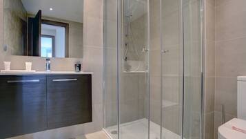 Un baño moderno con ducha acristalada, muebles de madera oscura y un inodoro blanco.