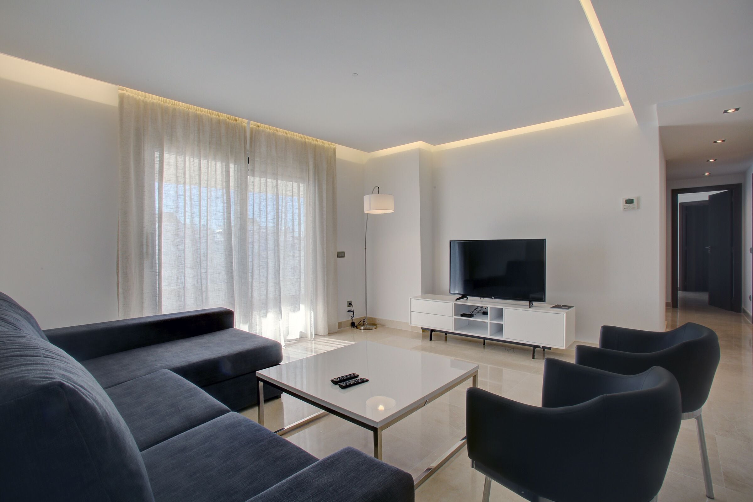 Un saló modern amb un sofà, una taula de centre, una televisió i una làmpada.