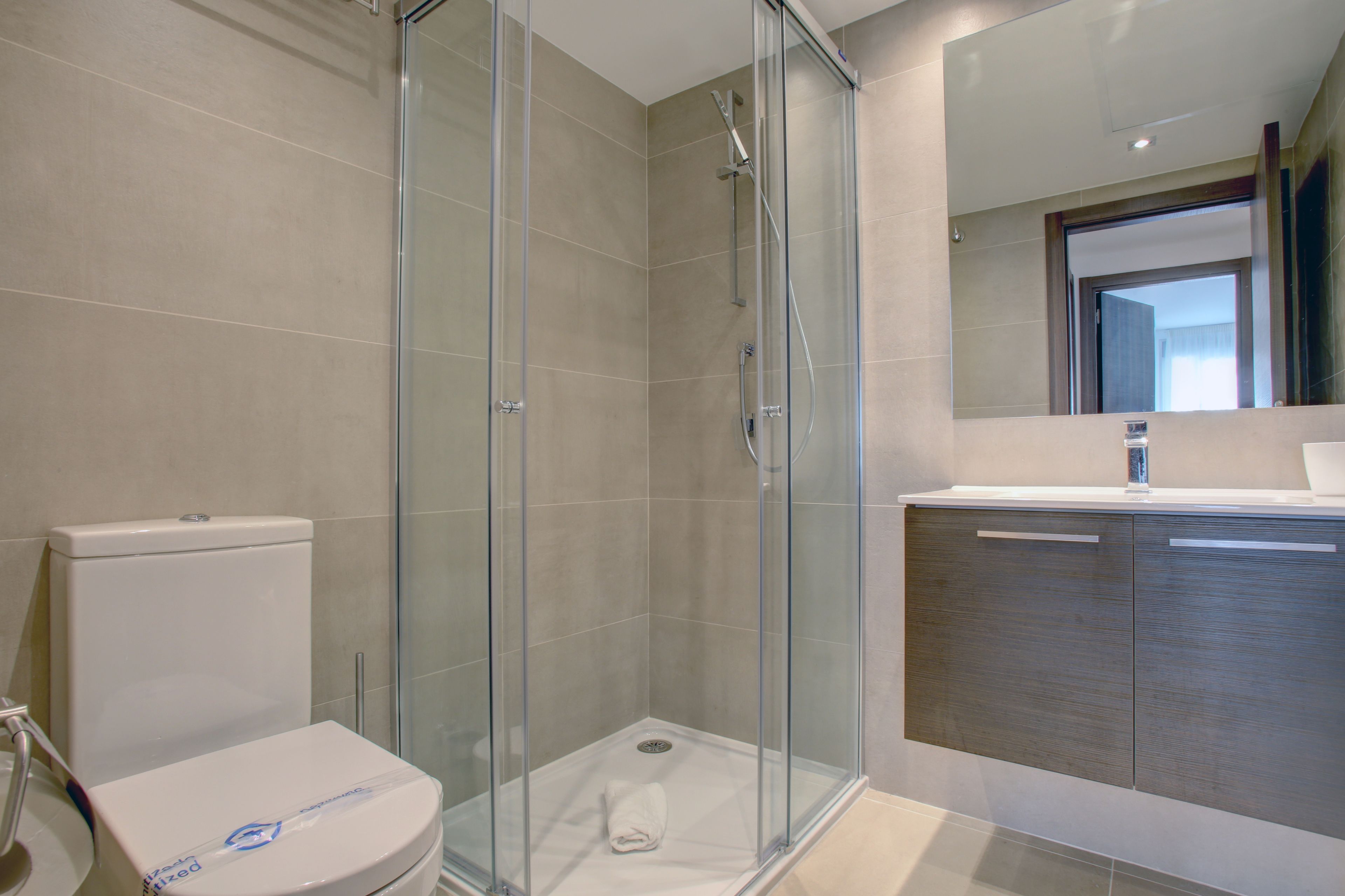 Een moderne badkamer met een glazen douchecabine, toilet en een wastafel met spiegel.