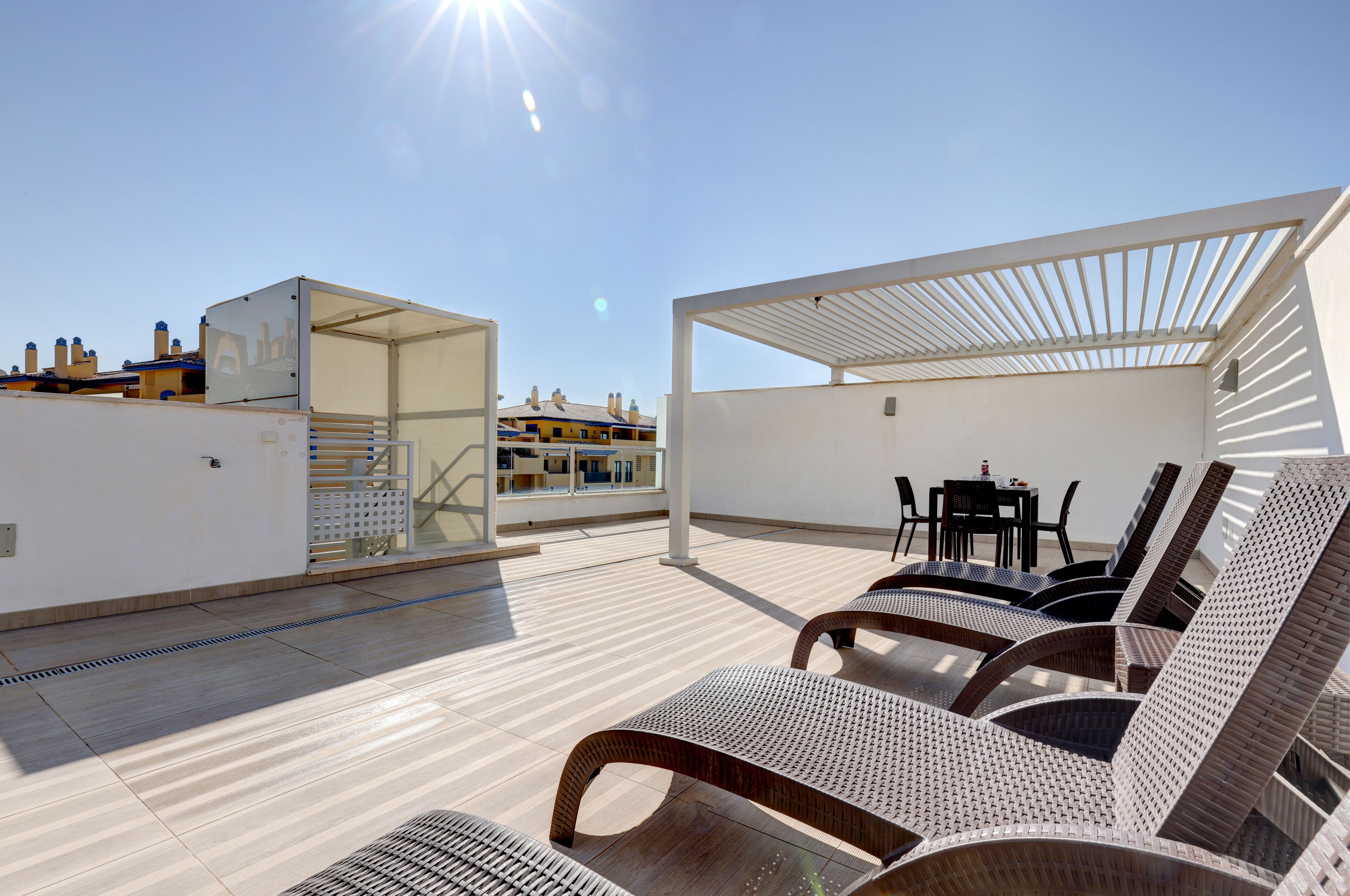 A rooftop terrace with sun loungers, a table, and chairs.