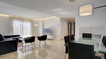 A modern living room with a glass dining table, black chairs, a dark sofa, and a TV.