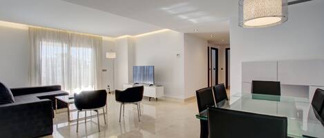 A modern living room with a glass dining table, black chairs, a dark sofa, and a TV.