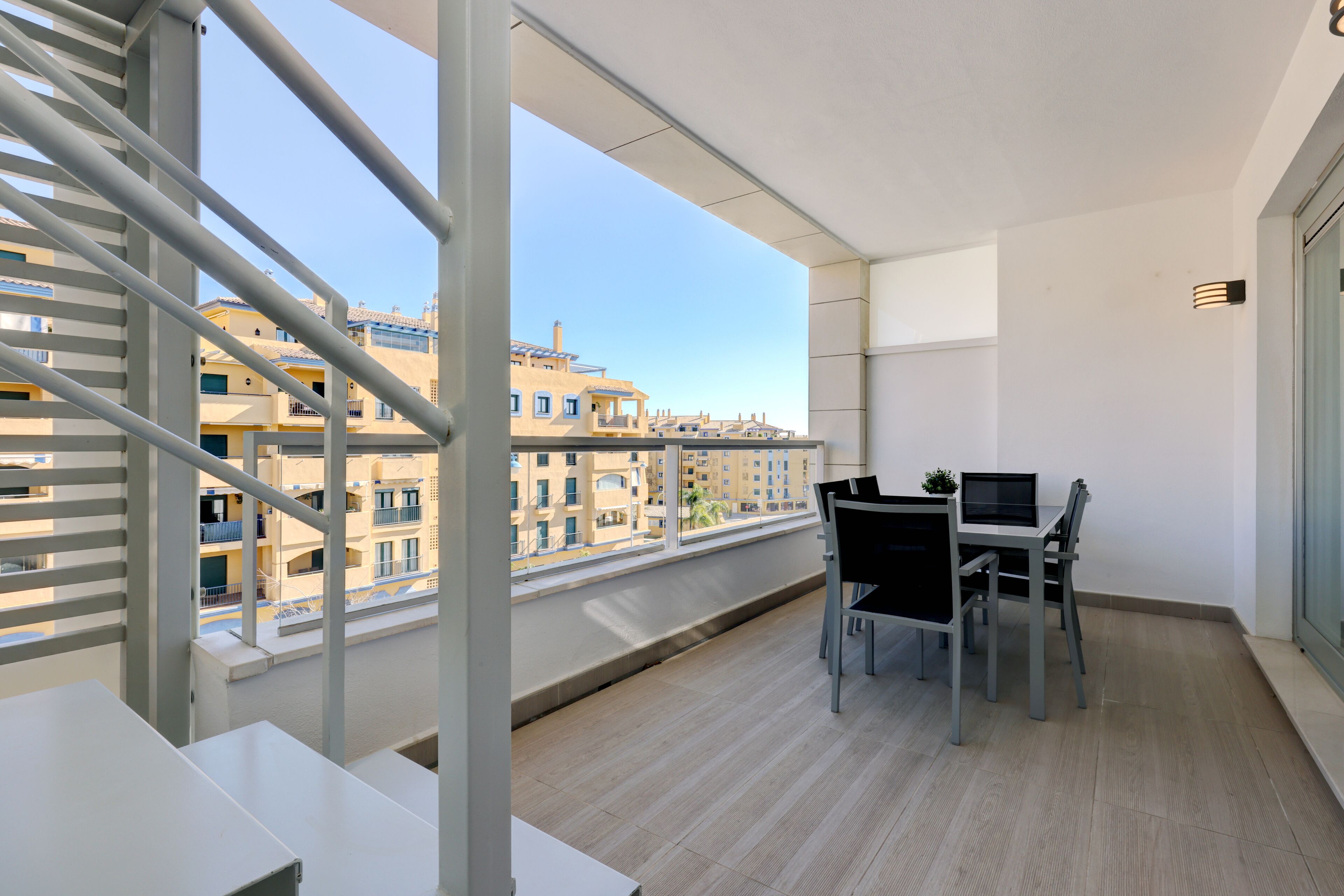 A balcony with a view of buildings, a table with chairs, and a window with blinds.