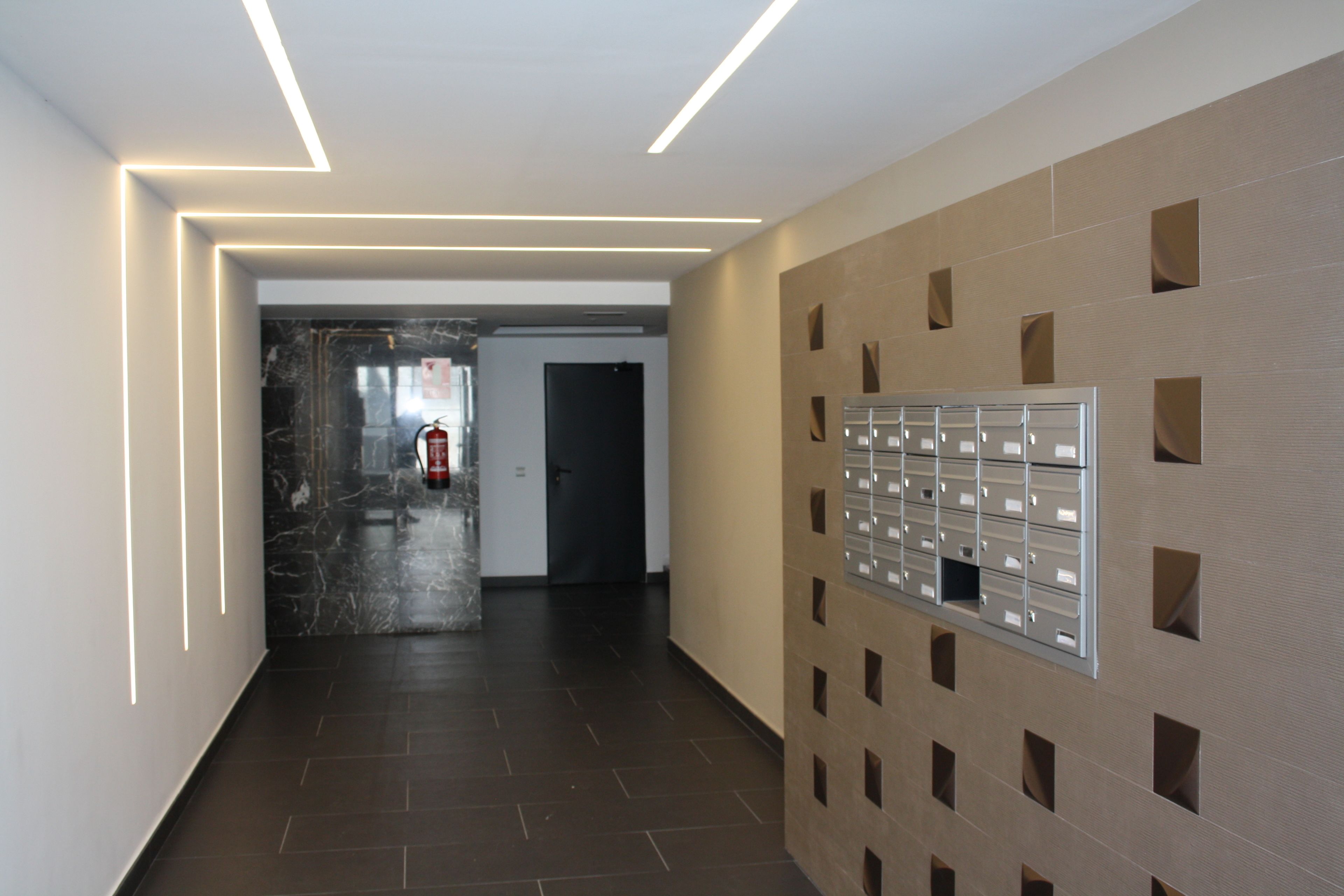 A modern hallway with a marble floor, a fire extinguisher, and a wall-mounted mail slot.