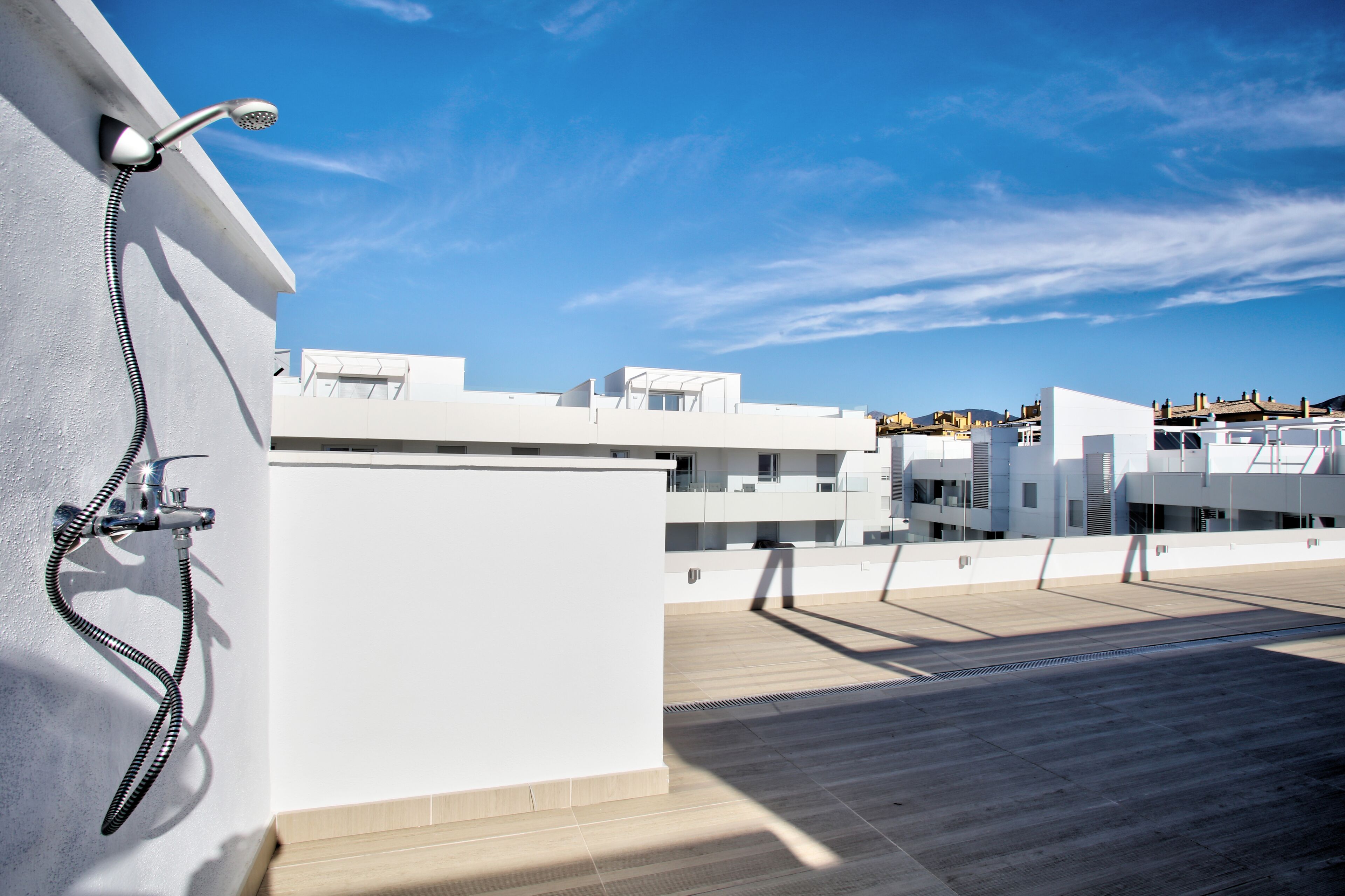 Eine Dachterrasse mit Brause, blauem Himmel und modernen weißen Gebäuden im Hintergrund.