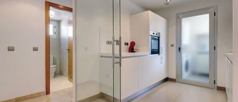 A modern kitchen with a glass partition, a built-in oven, and a red kettle.