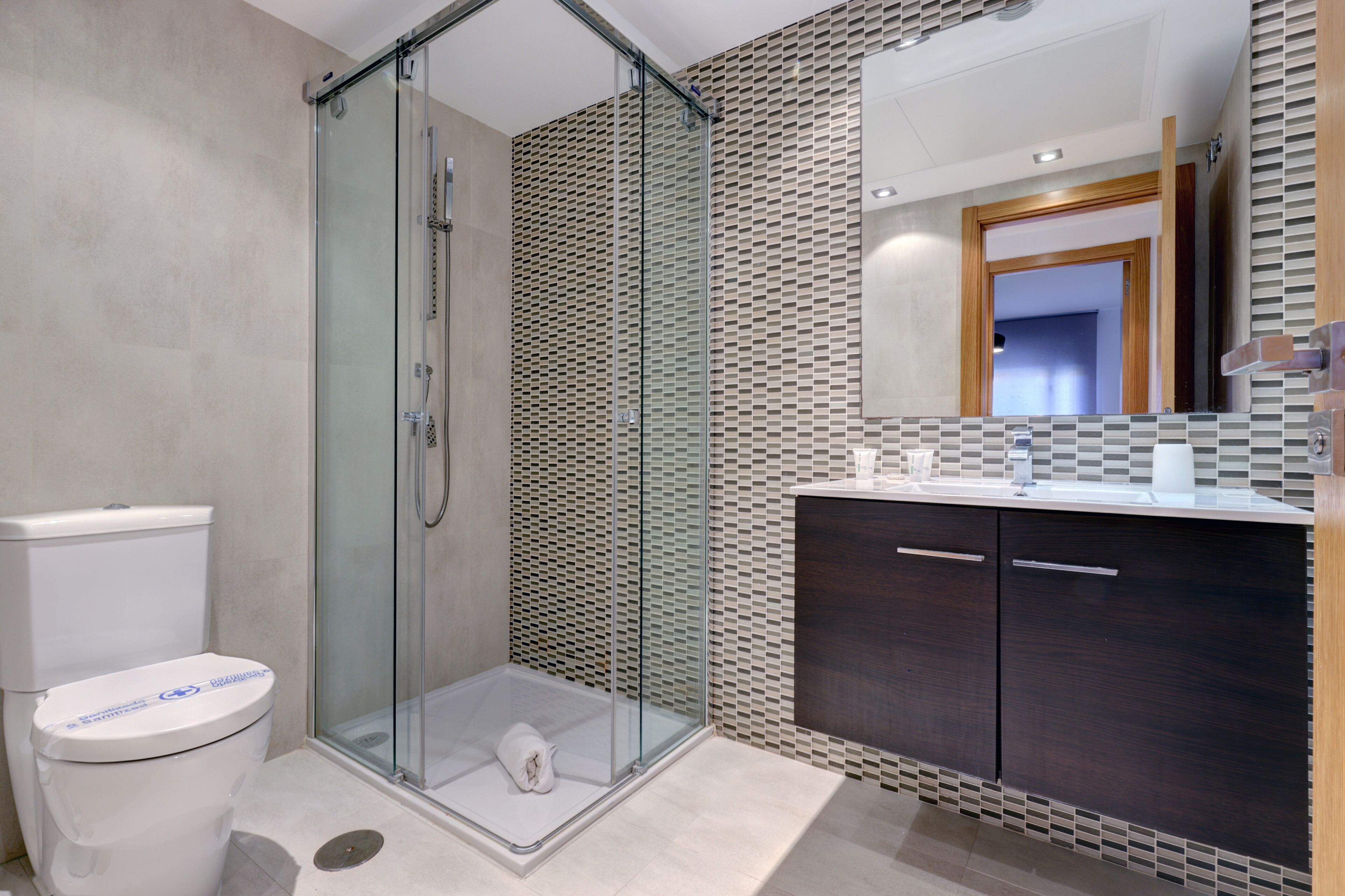 Un bagno moderno con doccia vetro, un water e un mobile lavabo con armadietti in legno scuro.