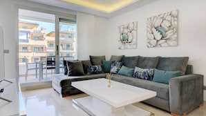 A modern living room with a grey sofa, white coffee table, and two floral paintings on the wall. - Aqua Apartments Vento, Marbella (Marbella)