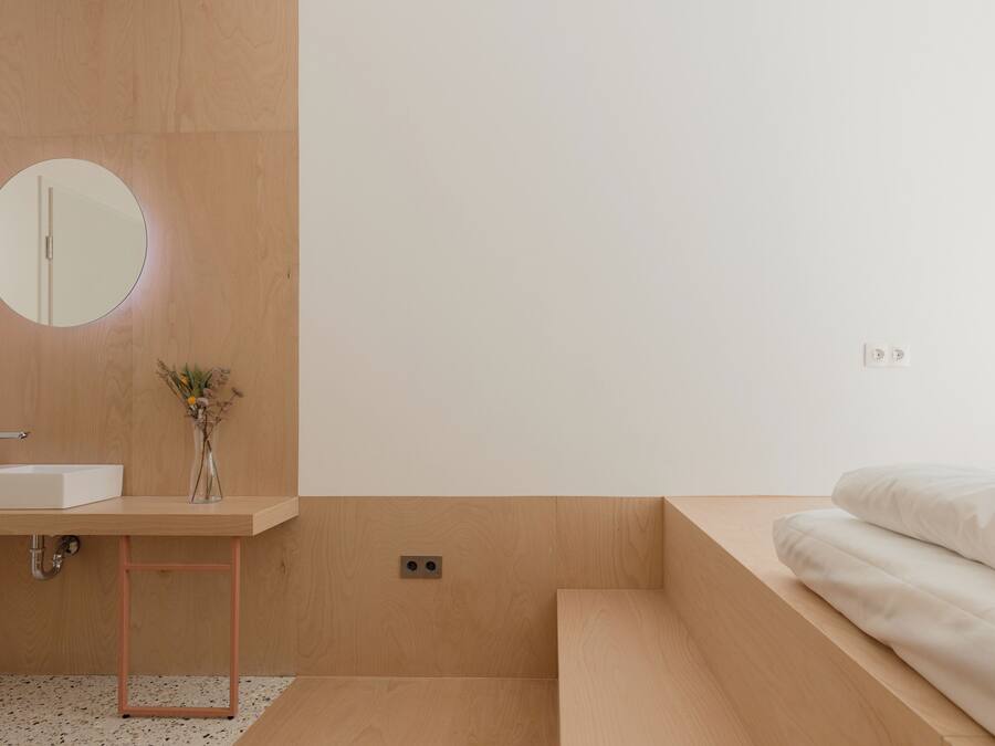 A modern bathroom with a wooden vanity, a round mirror, and a small vase with dried flowers.