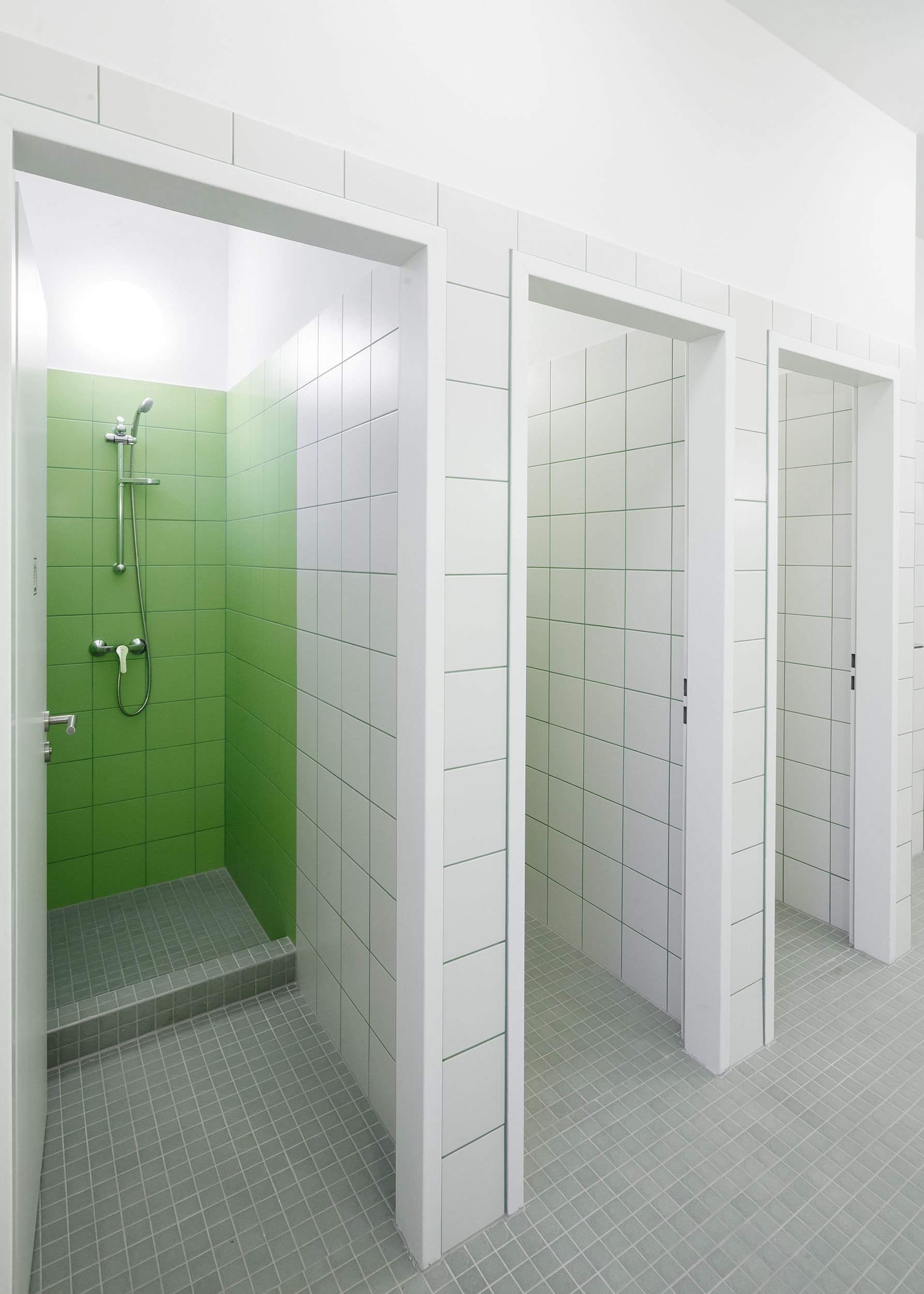 A modern bathroom with green and white tiled walls, a shower area, and a tiled floor.