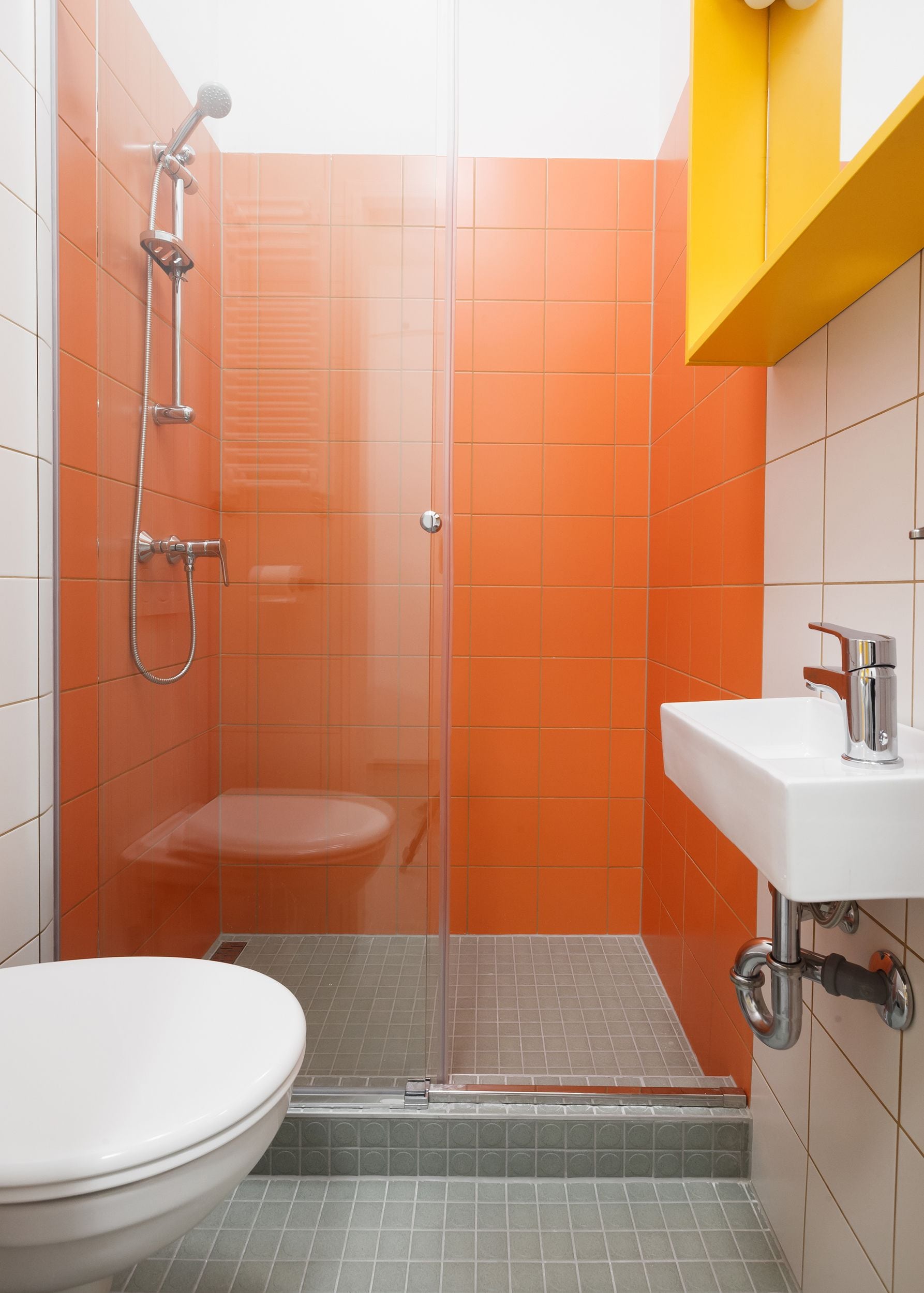 Ein Badezimmer mit einer orangefarben gefliesten Dusche, einer weißen Toilette und einem Waschbecken mit Armatur aus Chrom.