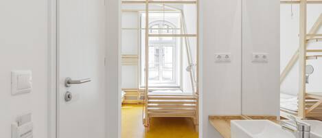 A modern bathroom with a wooden bench, a large mirror, and a yellow floor.
