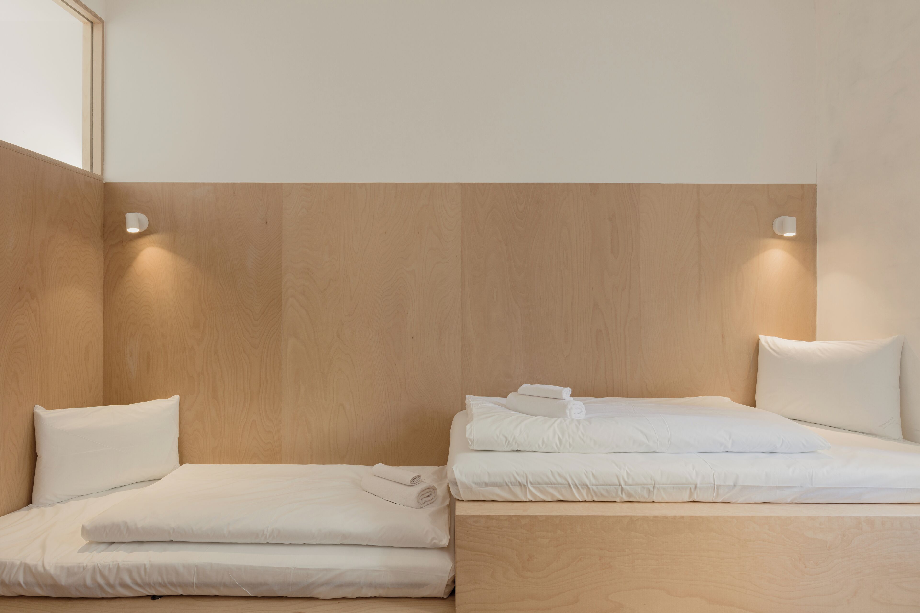 Una camera d'albergo con due letti, testiere in legno e illuminazione a parete.