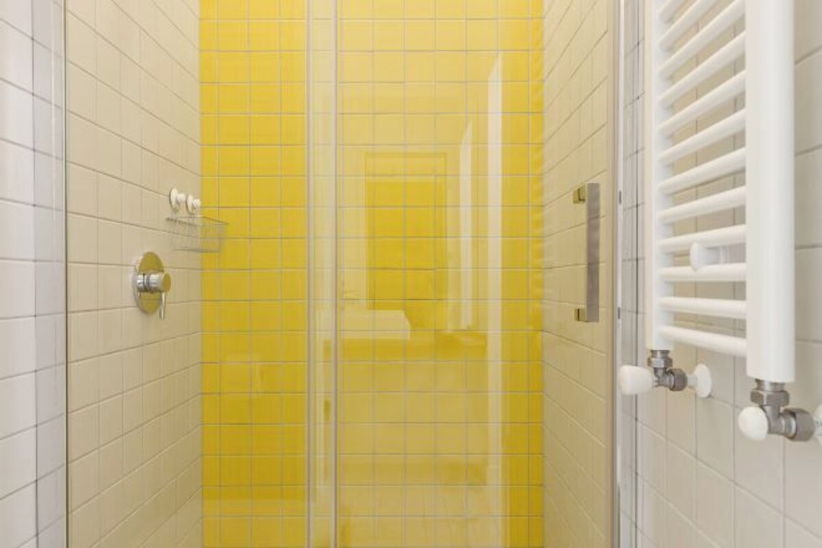 Une salle de bain avec des murs recouverts de carreaux jaunes, une douche en verre et un porte-serviettes blanc.
