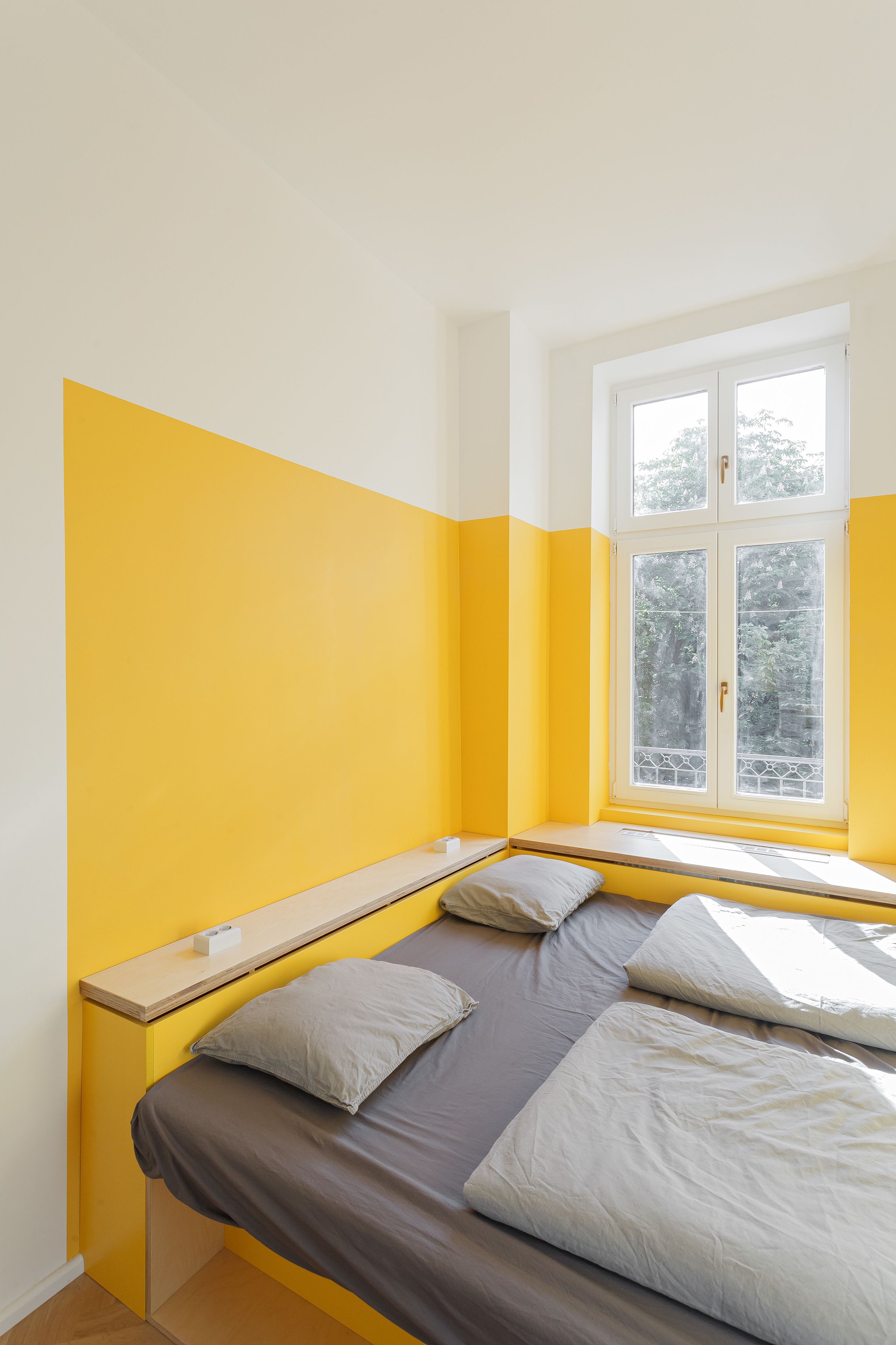 Una habitación con una cama, una ventana y una pared amarilla.
