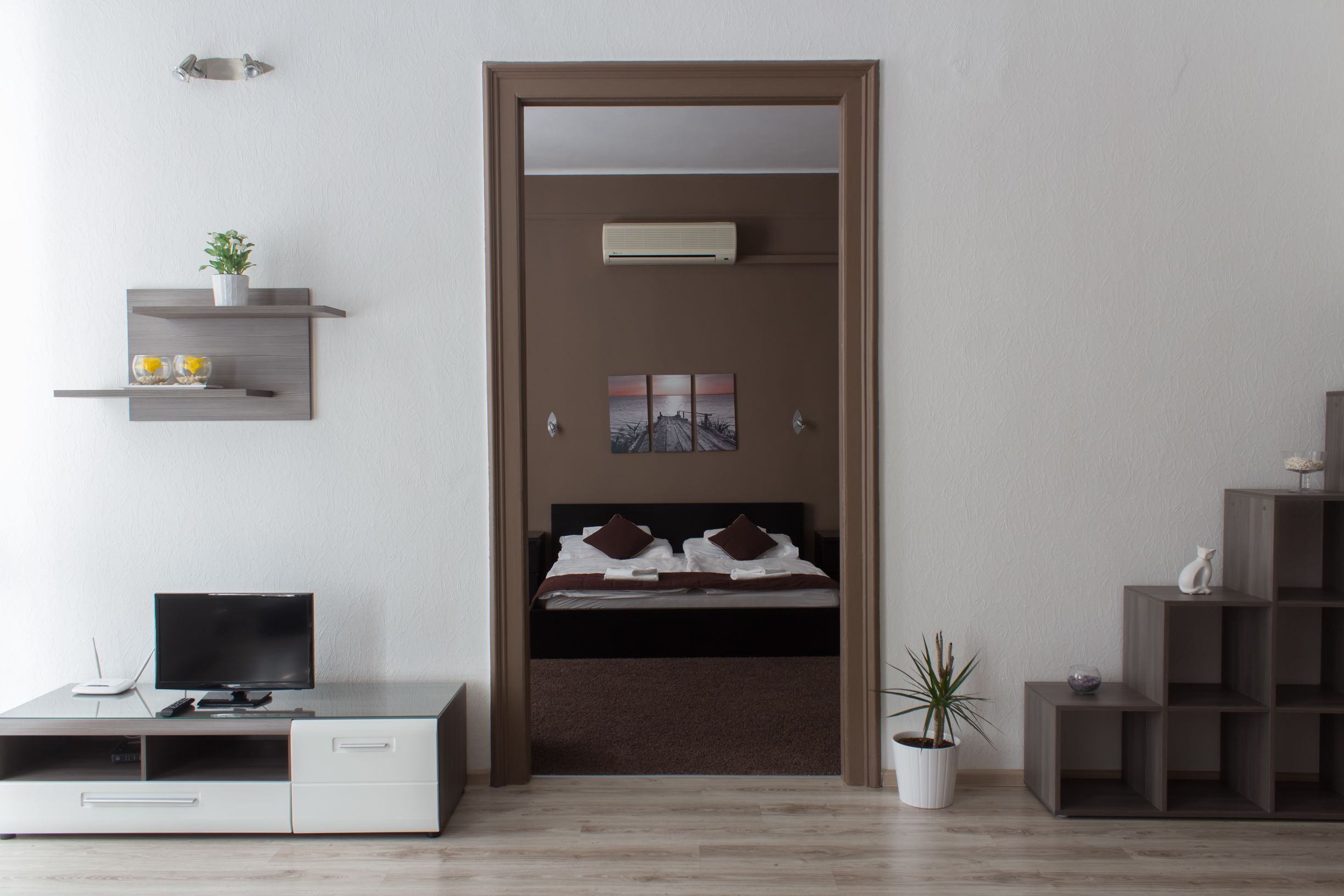 A modern bedroom with a bed, a TV, a desk, and a potted plant.