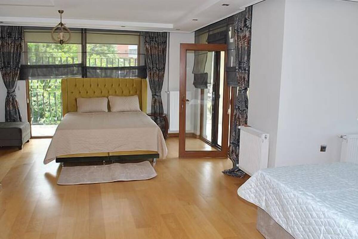 A bedroom with a large bed, a window with curtains, a radiator, and a door leading to a balcony.