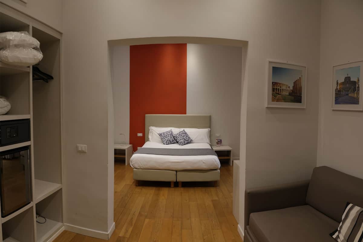 A modern bedroom with a bed, a nightstand, a wardrobe, and a sofa.