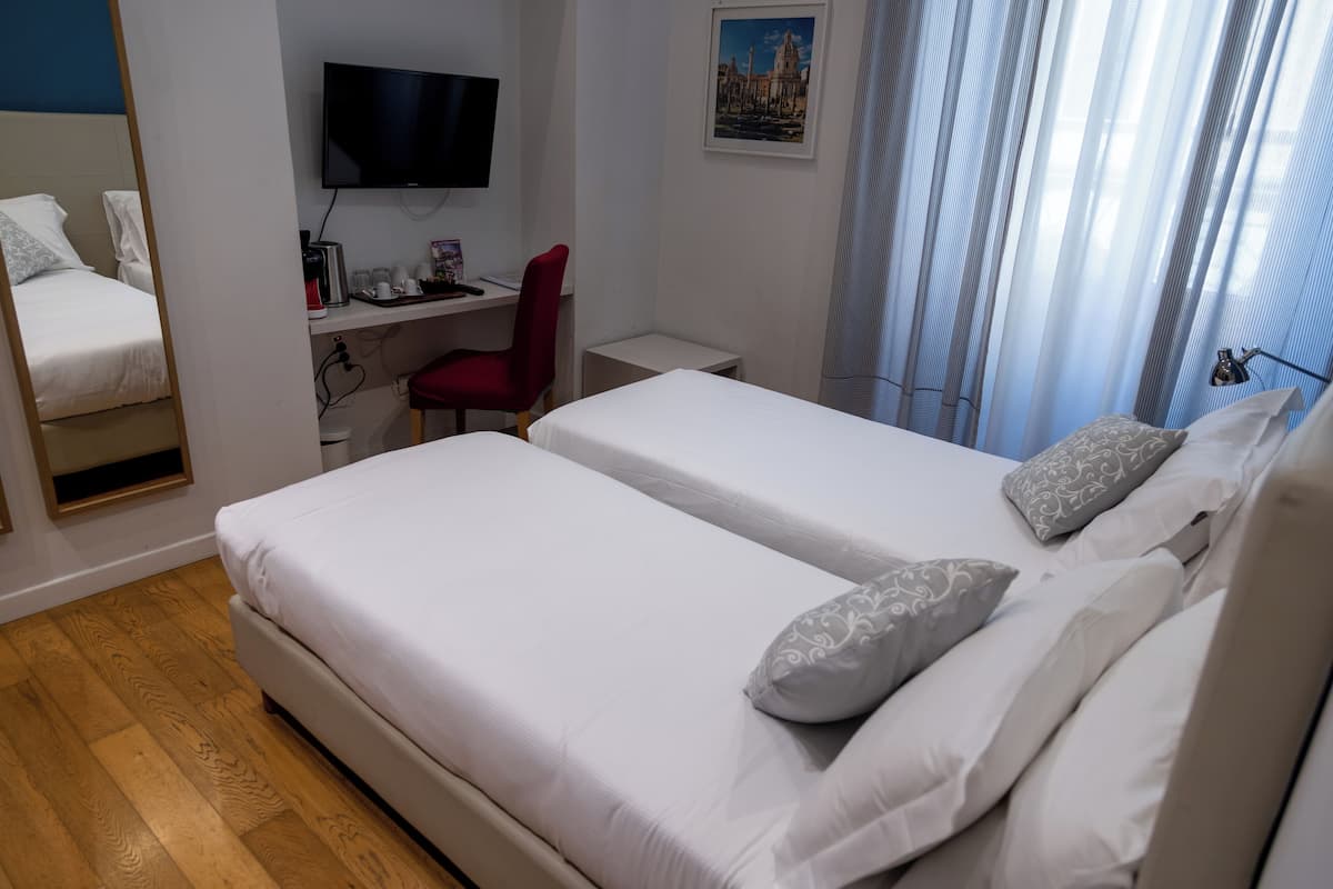 A hotel room with two beds, a desk with a chair, a TV, and a window with curtains.