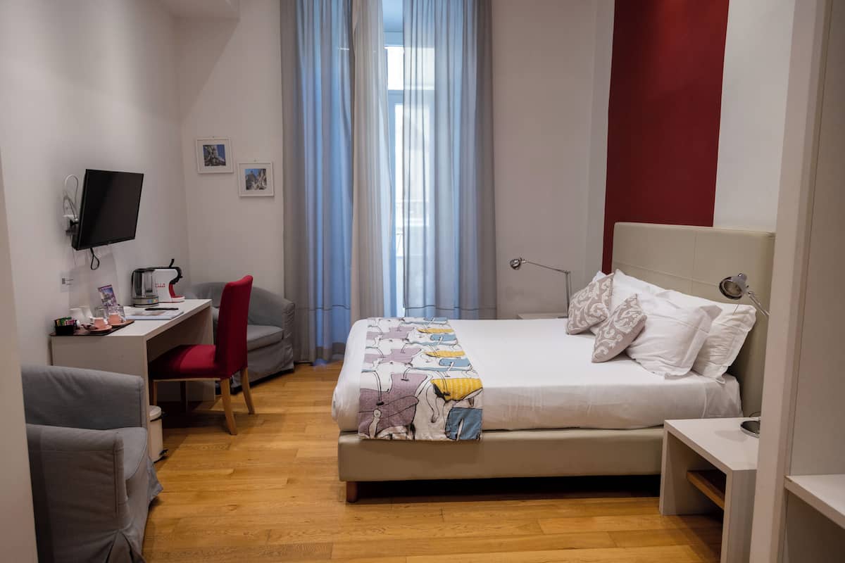 A modern hotel room with a bed, desk, chair, and a TV.