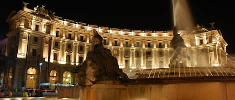 A grand building with a large fountain in front, featuring two statues and a water jet.