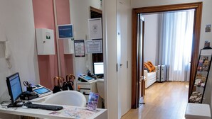 A modern office space with a desk, computer, and office chairs. There is a hallway leading to a bedroom with a bed and a window. - Sofia's Suites Guesthouse (Rome)