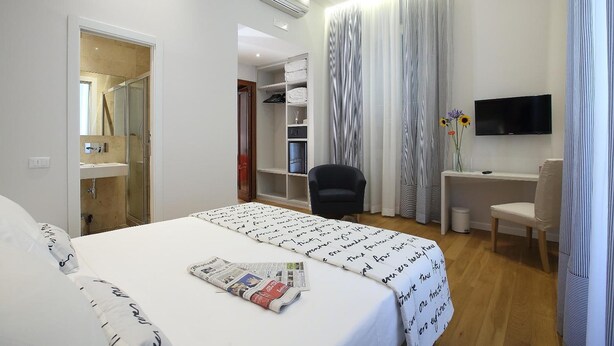 A hotel room with a bed, a desk, a chair, a TV, and a bathroom visible through an open door. - Sofia's Suites Guesthouse (Rome)