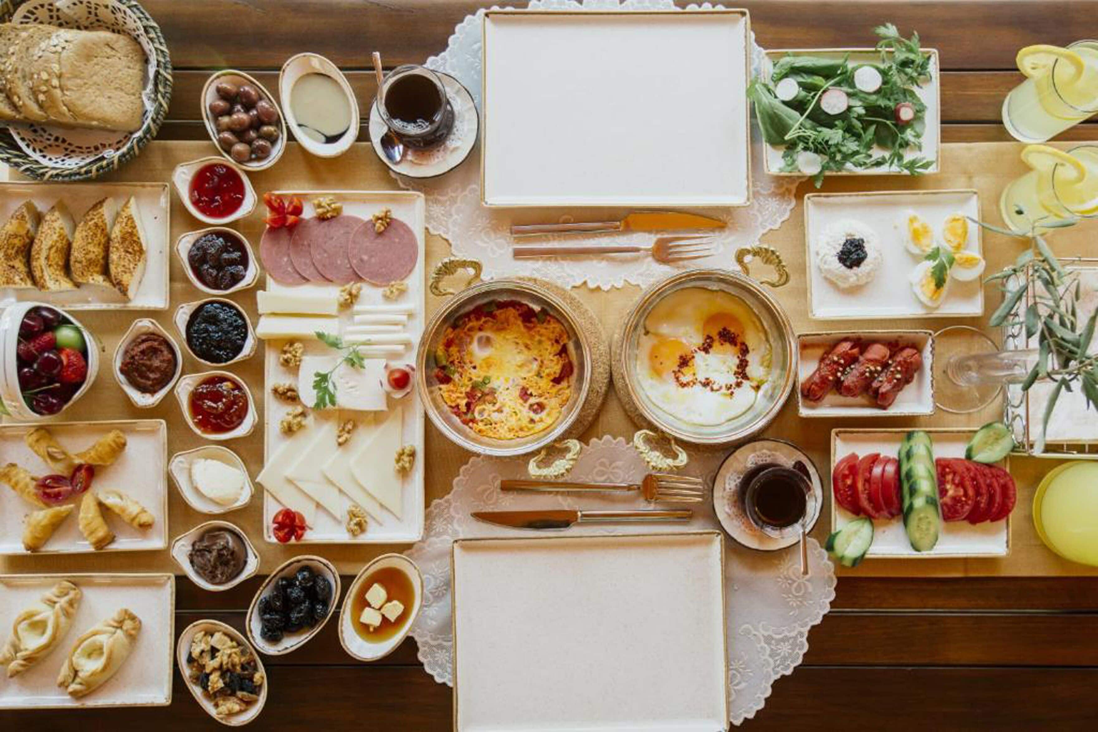 A table set with various food items including bread, cheese, meats, and fruits, arranged on a wooden table with a lace doily.