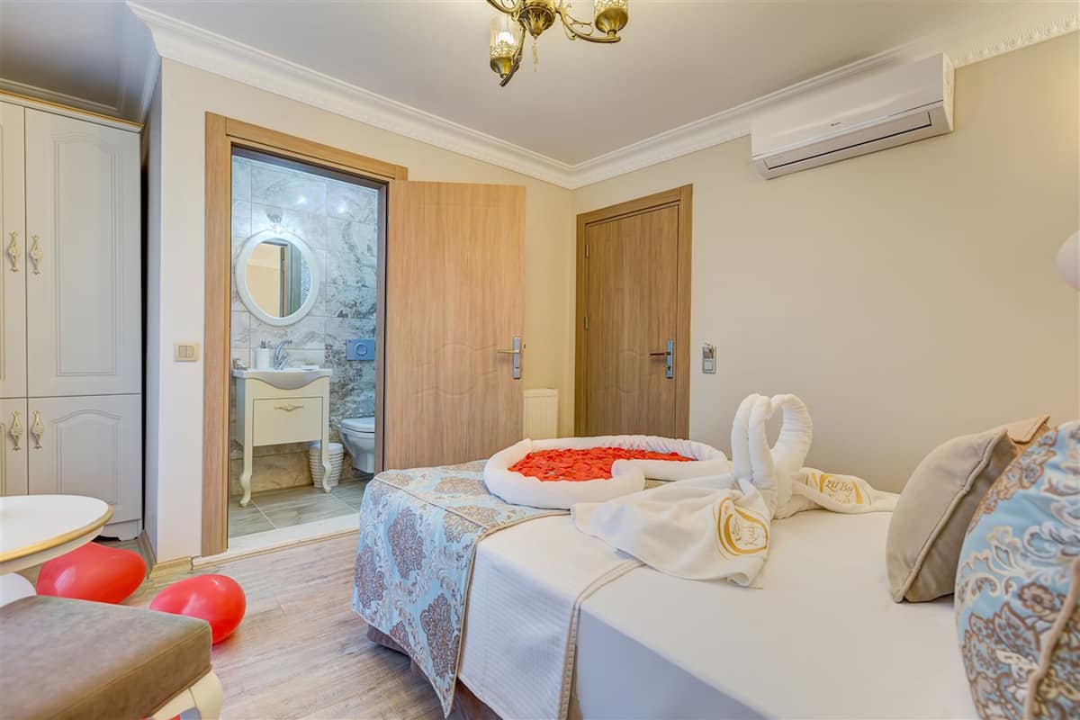 Un dormitorio con cama, mesita de noche, espejo, armario y un baño visible a través de una puerta abierta.