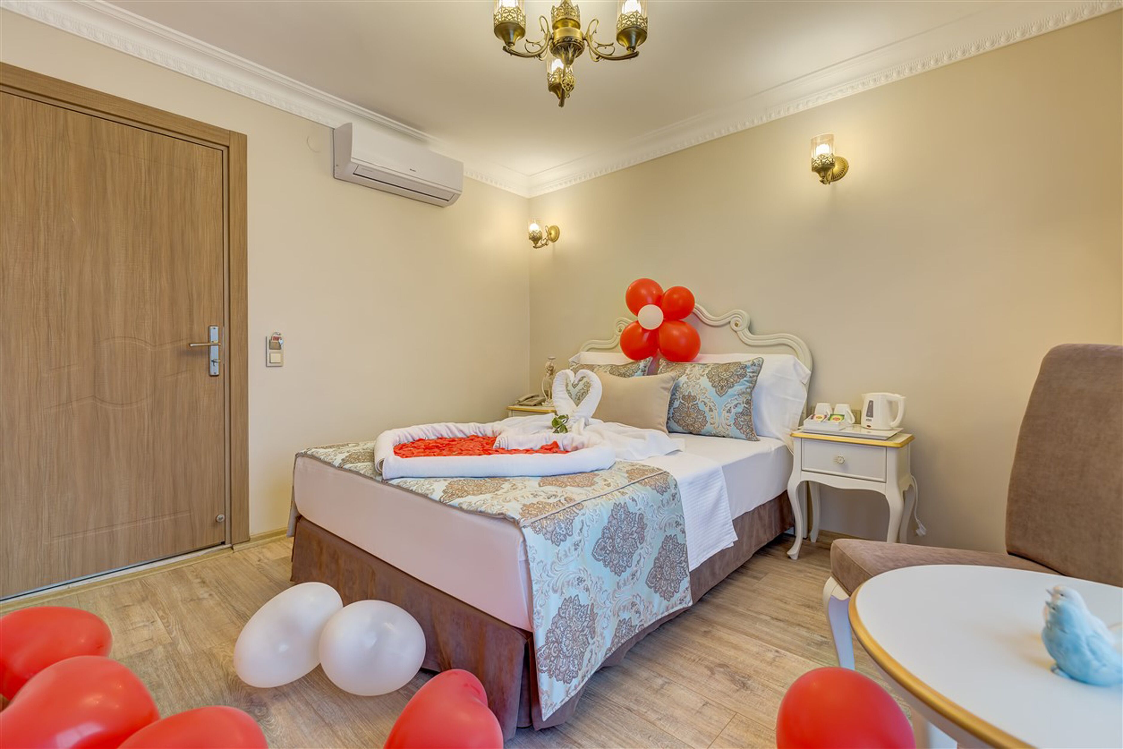 Habitación de hotel con cama, mesita de noche, silla y una pequeña mesa con un pájaro.
