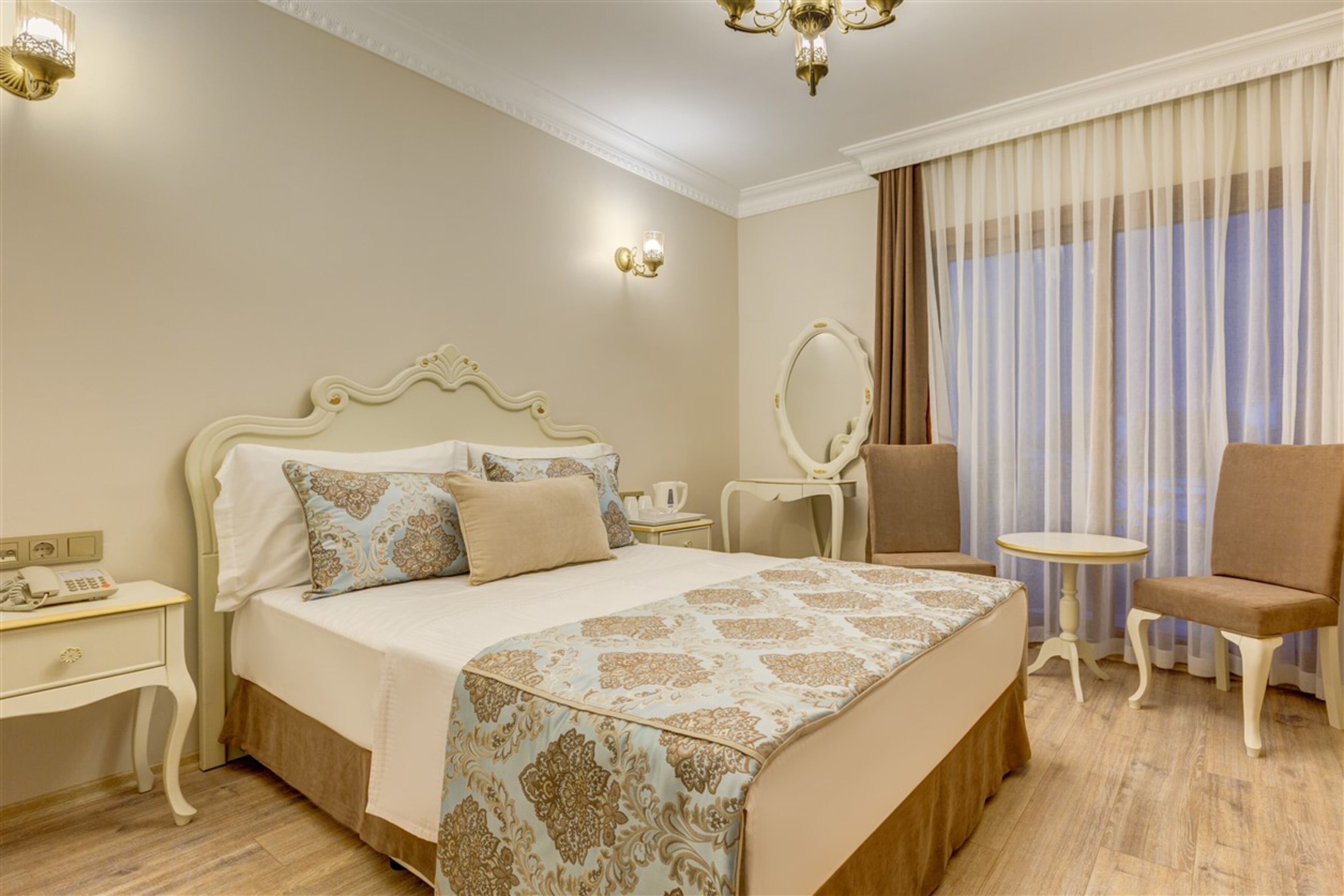 Een hotelkamer met een groot bed, een nachtkastje met een lamp, een stoel, een klein rond tafeltje en een spiegel.
