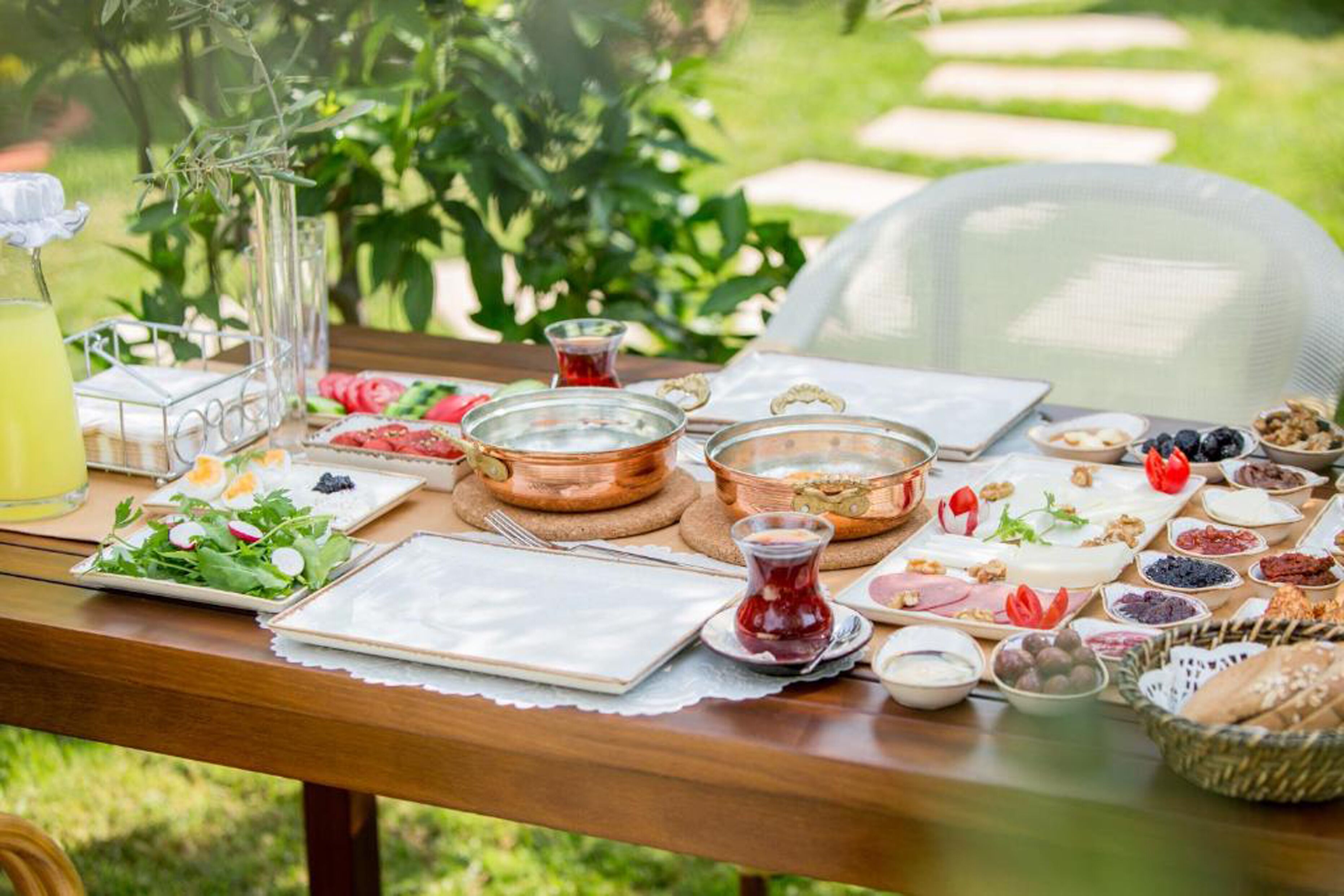 A table set outdoors with various food items, including fruits, cheeses, and a glass of juice.