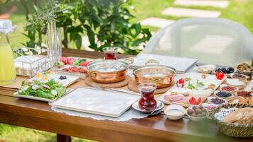A table set outdoors with various food items, including fruits, cheeses, and a glass of juice.