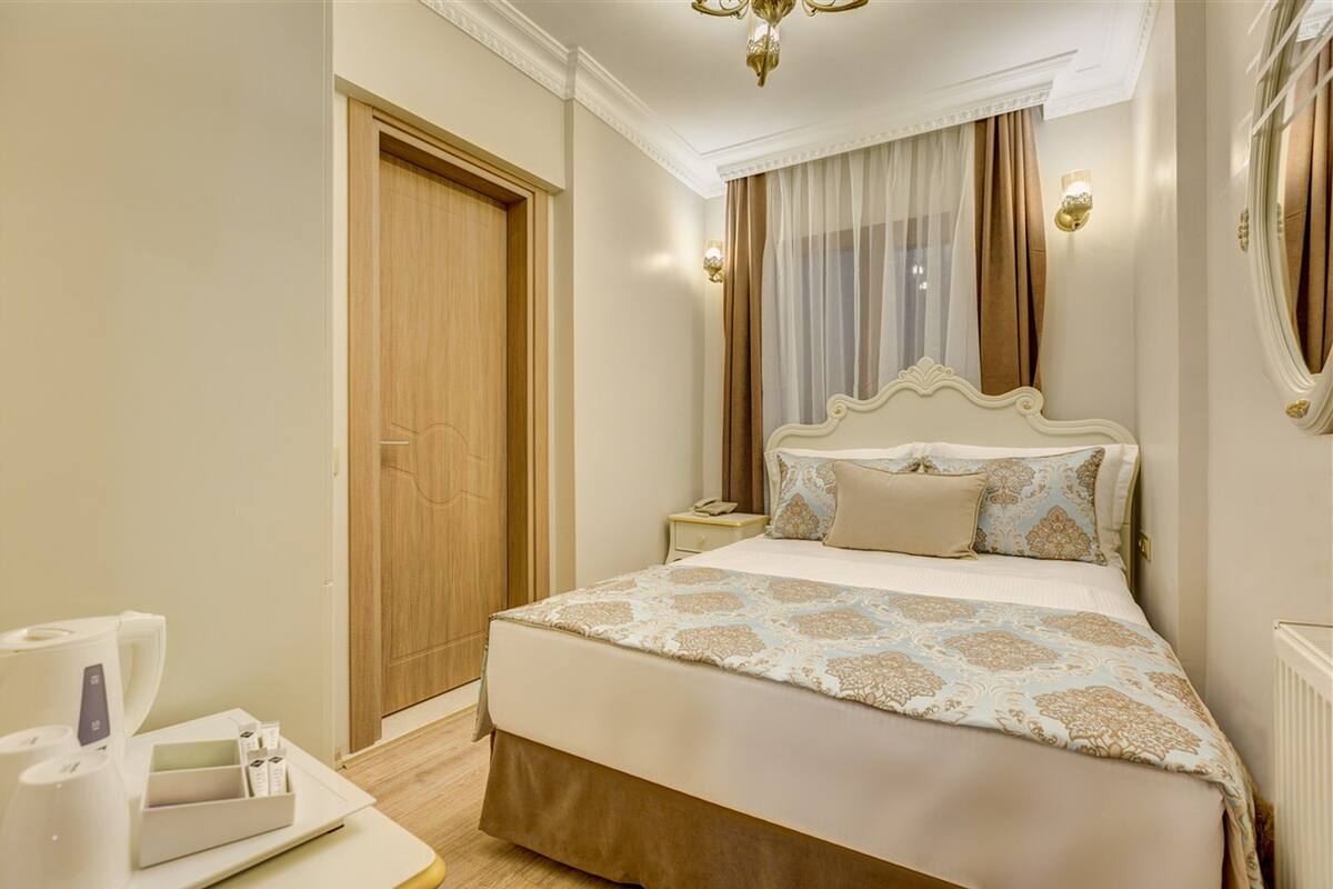 Habitación de hotel con una cama grande, una mesita de noche, un espejo, una lámpara de araña y una puerta.