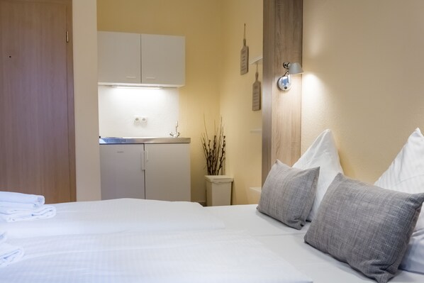 Une chambre d’hôtel comprenant un lit, une petite kitchenette, une table de chevet et une lampe fixée au mur.