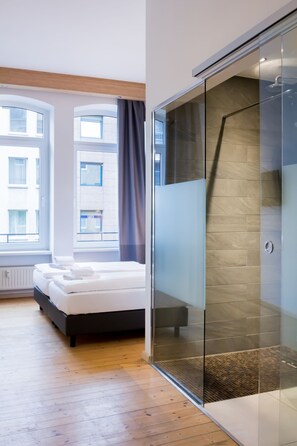 A modern hotel room with a bed, a glass shower enclosure, and large windows. - dingdong koblenz - city apartments (Koblenz)