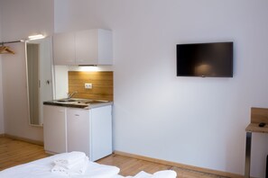 Et lille værelse med tekøkken, fladskærms-TV og en seng med pænt foldede håndklæder.