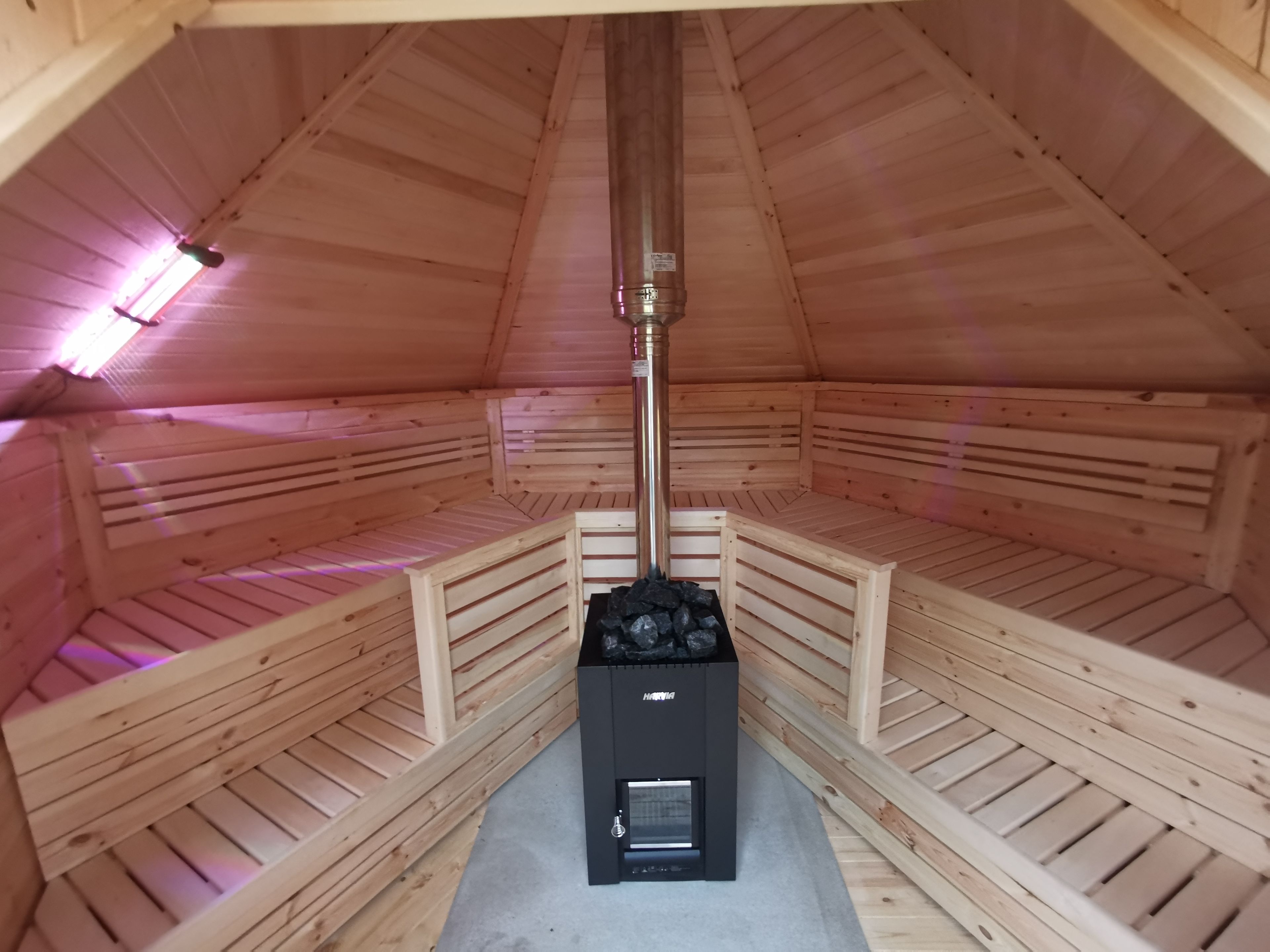 Un cuarto de sauna con bancos de madera, un calentador central y un techo inclinado.