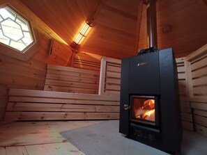 A wood-burning stove in a cabin with a window and wooden walls. - Hennetaler Hof (Eslohe)
