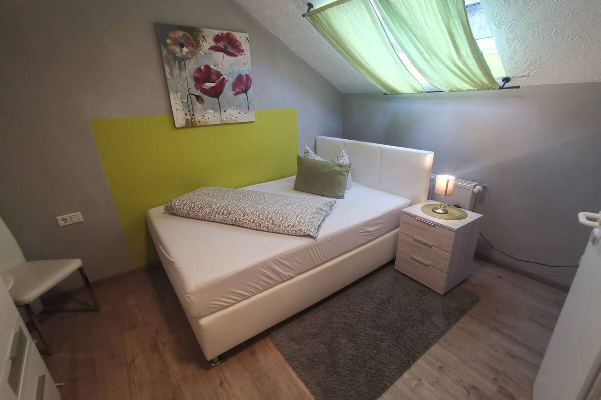 A bedroom with a bed, bedside table, lamp, and a painting on the wall.