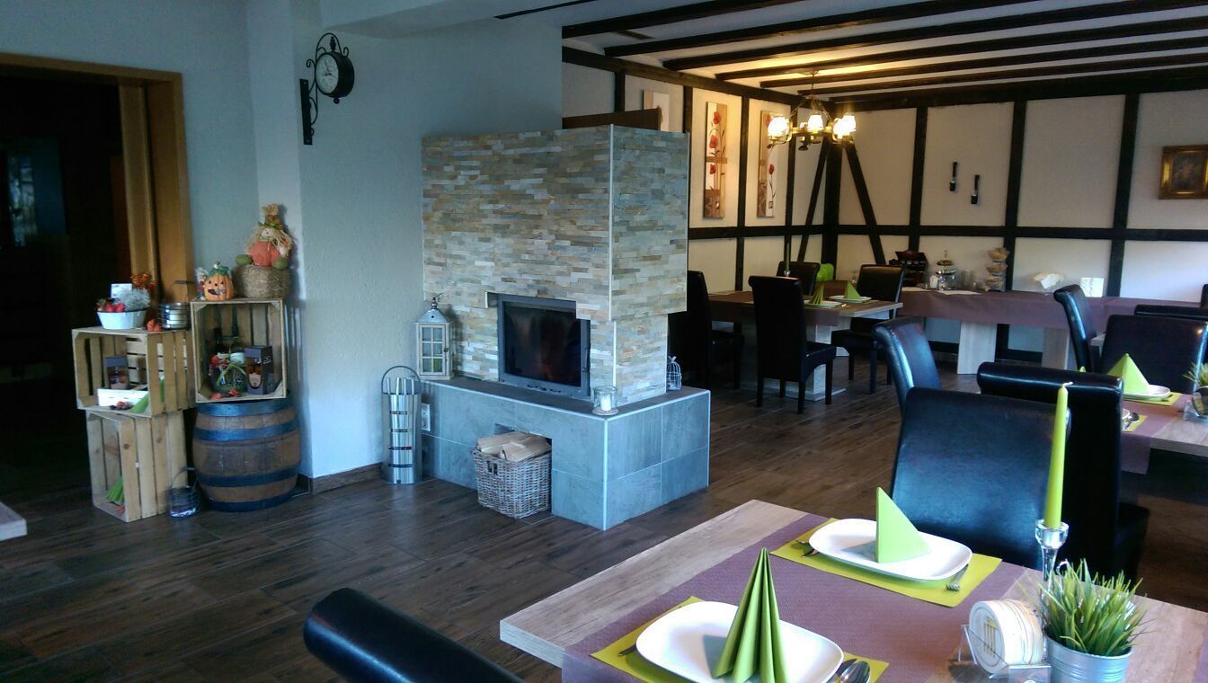 Un salon chaleureux avec une cheminée en pierre, des meubles en bois et un coin repas avec une table mise pour deux personnes.