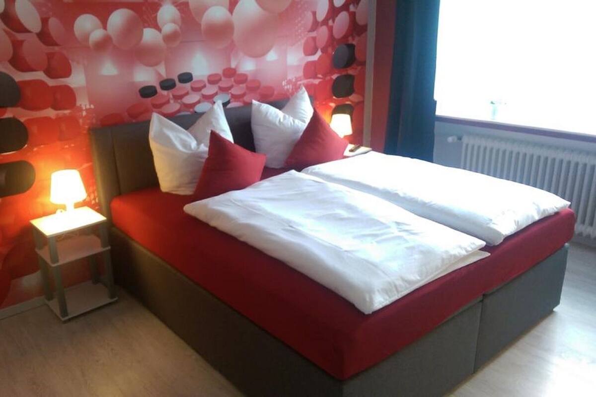 A modern bedroom with a bed, pillows, a nightstand, and a wall with a unique pattern.