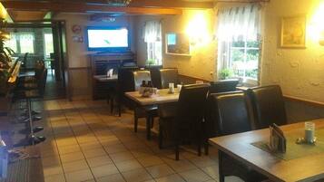 Um restaurante com várias mesas e cadeiras, uma televisão e uma janela com cortinas.