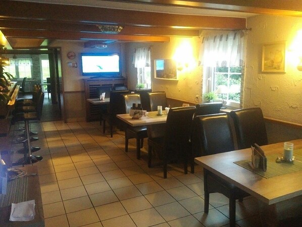 A restaurant with multiple tables and chairs, a television, and a window with curtains. - Hennetaler Hof (Eslohe)