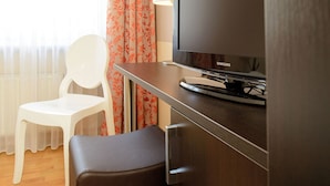 A hotel room with a television on a wooden stand, a white chair, and a small table. - Hotel Europa (Bonn)