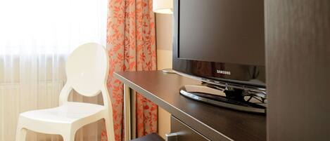 A hotel room with a television on a wooden stand, a white chair, and a small table.